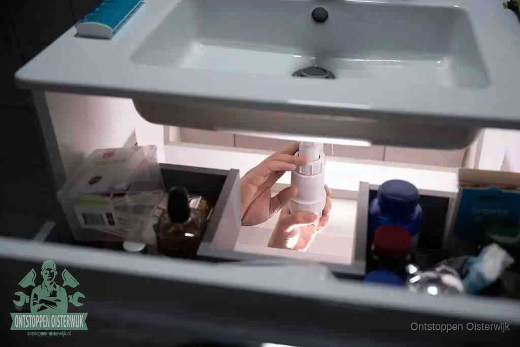 Een pompfles met zeep boven een wastafel, de heet water en afwasmiddel-methode om een vetprop in de afvoer los te maken in Oisterwijk