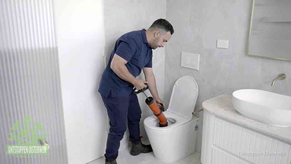 Een monteur buigt over een wandcloset en duwt met de hand een persluchtontstopper in de toiletpot om de verstopping handmatig los te maken in Oisterwijk