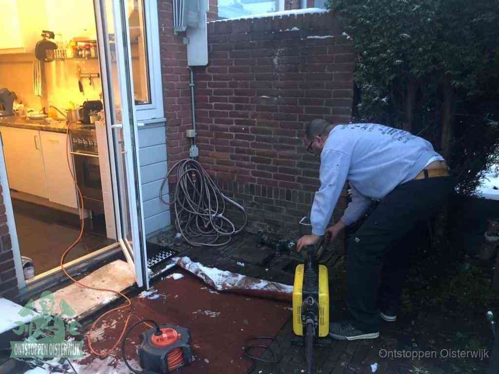 Een monteur werkt buiten bij een open riool-/grondput met een elektrische ontstoppingsmachine om een verborgen afvoerprobleem op te sporen in Oisterwijk