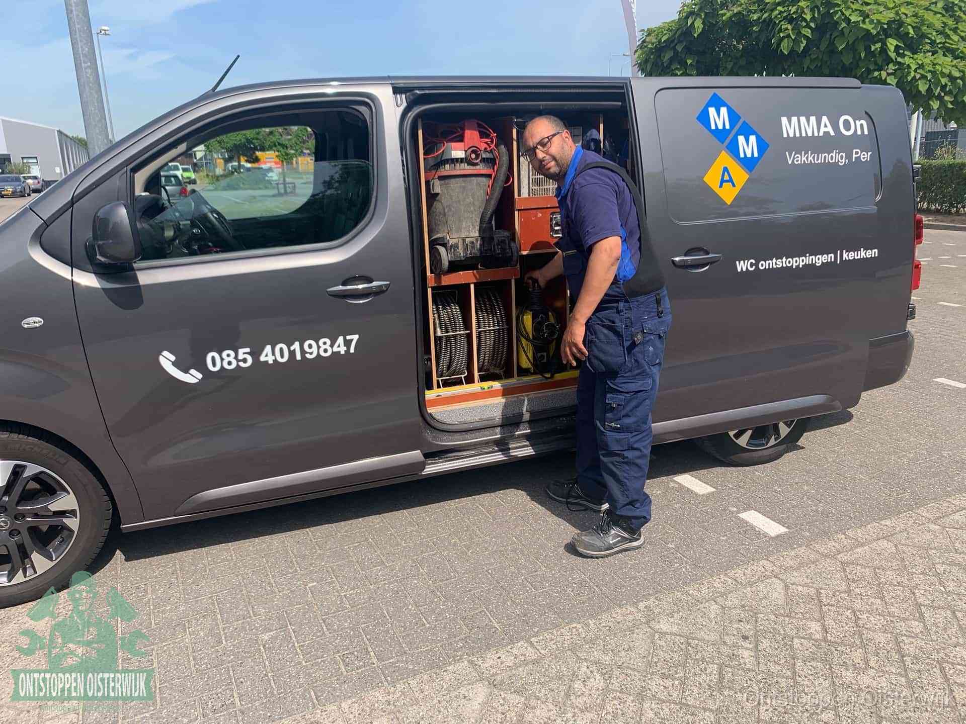 Een monteur bij de open schuifdeur van zijn bedrijfsbus op een parkeerplaats, klaar om de oorzaak van terugkerende afvoerverstoppingen aan te pakken in Oisterwijk