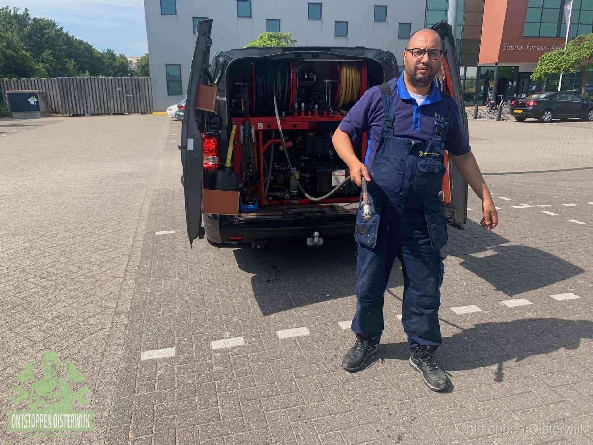 Een monteur bij zijn bestelbus met een hogedruk- en rioolreinigingsunit, klaar om de oorzaak van terugkerende wc-verstoppingen aan te pakken in Oisterwijk