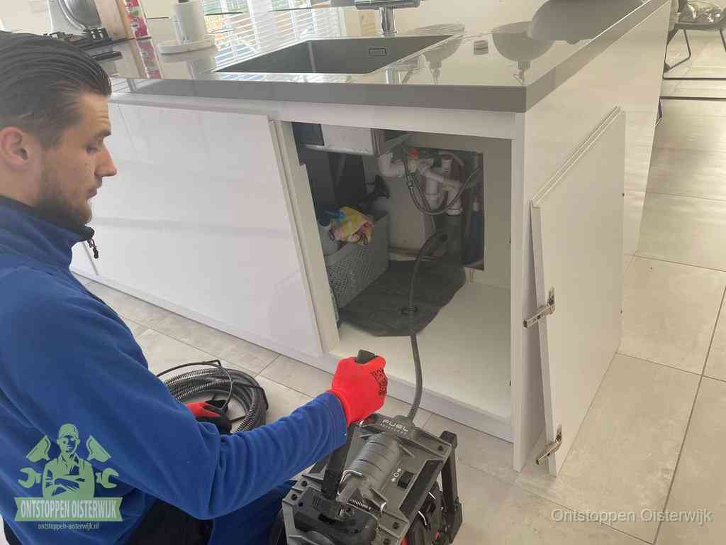 Monteur ontstopt met een veermachine een verstopte afvoer onder de gootsteen in Oisterwijk