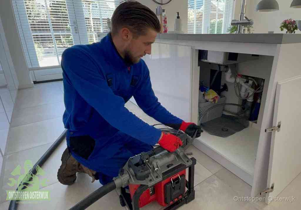 Een monteur voert een professionele elektrische ontstoppingsmachine in de afvoer onder de spoelbak tijdens het gootsteen ontstoppen in Oisterwijk